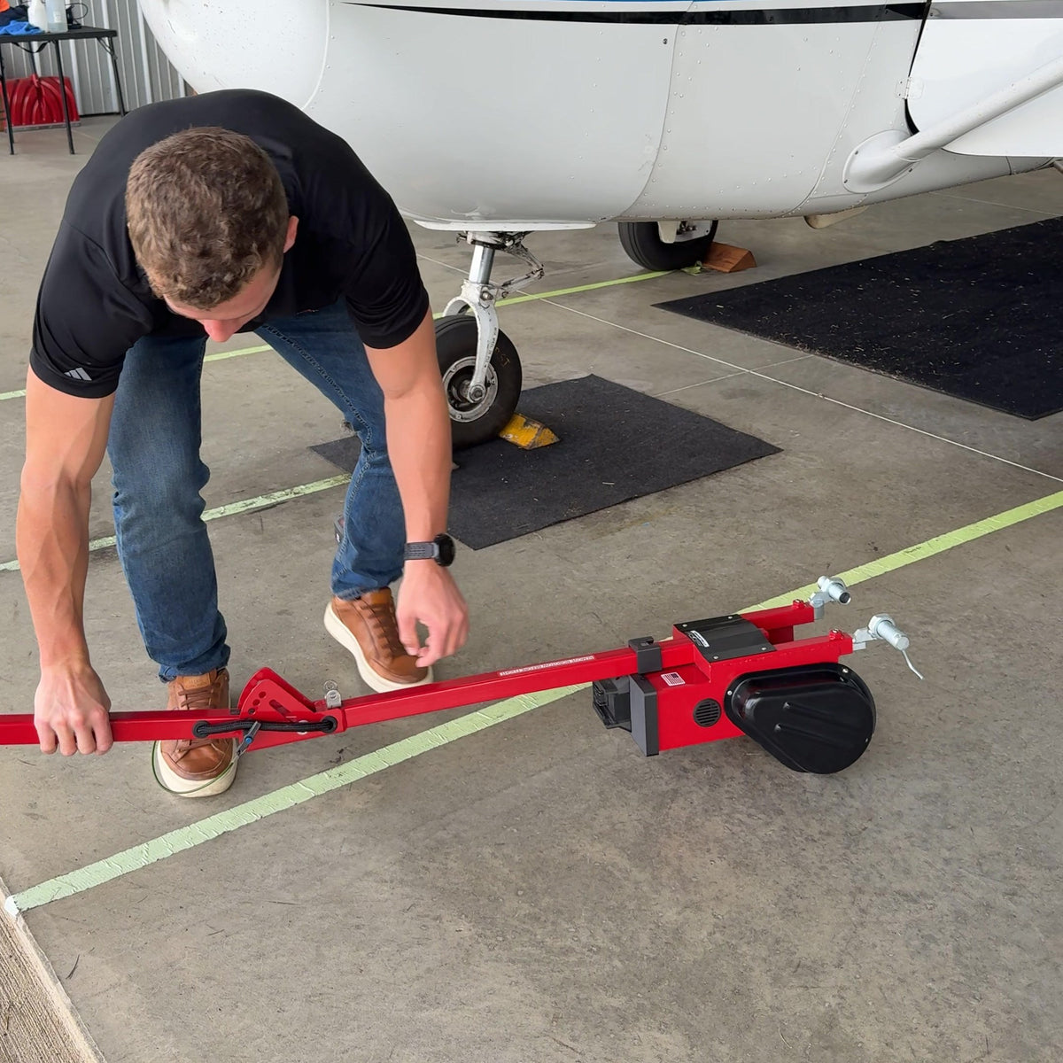 A person adjusting the pull handle of a Robotow 2.0 on a hangar floor in front of a plane's nose wheel.