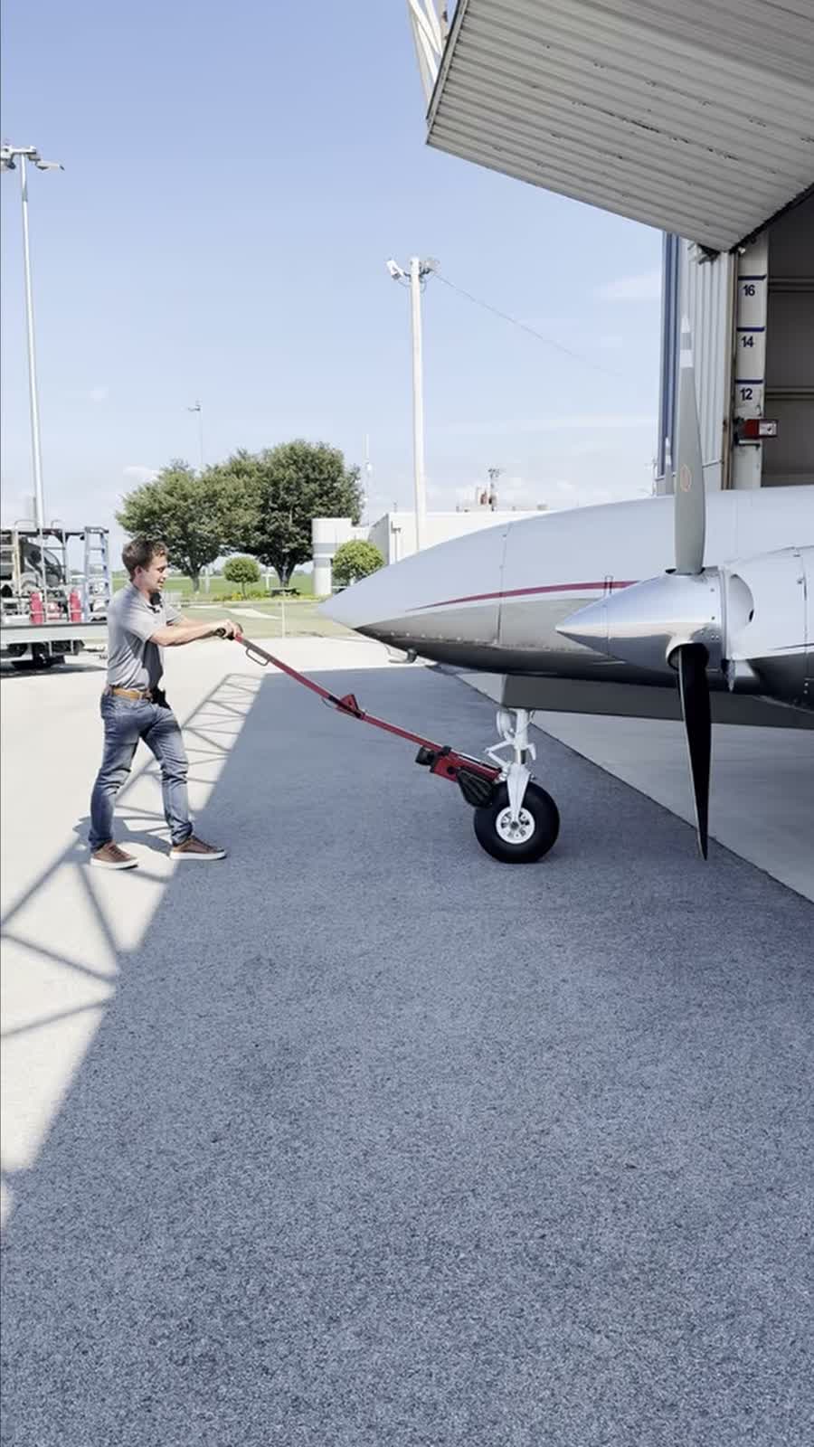 One person moving a twin at a hangar door, a Robotow at the nose wheel, both hands on the handle.