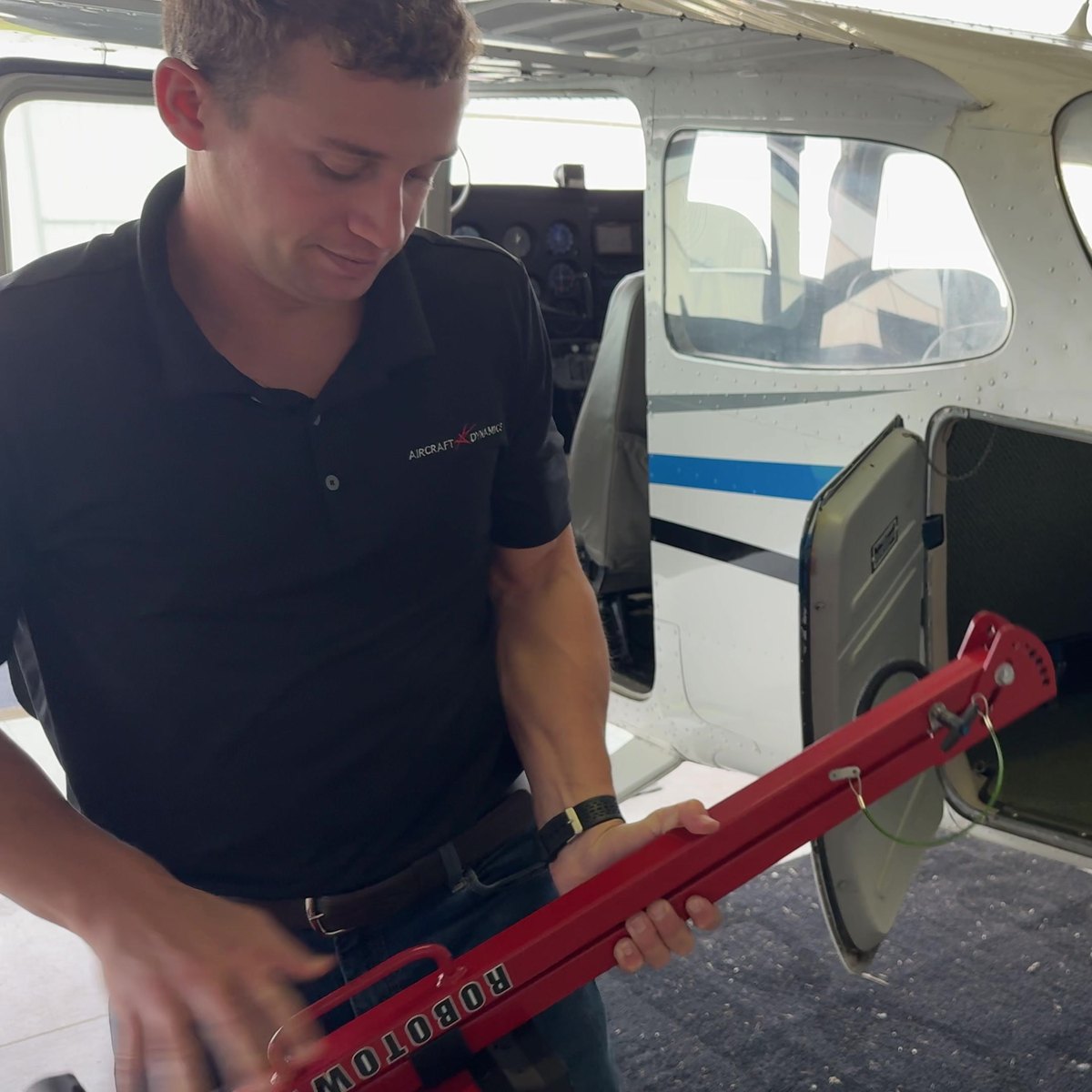 A folded Robotow 2.0 Pro frame held by its handle beside an open baggage door.