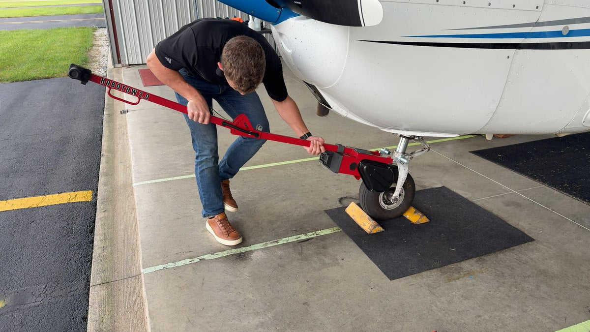A Robotow 2.0 Pro frame extended and hooked to an airplane nose wheel, one person at the handle.